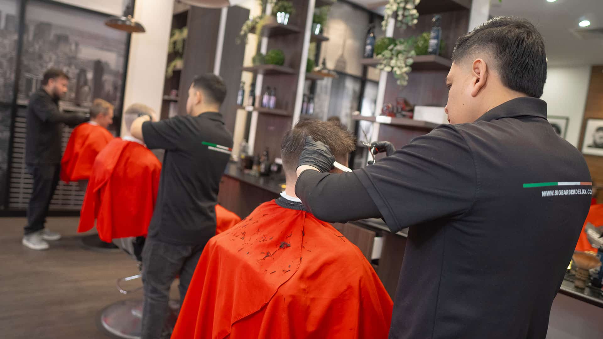 Expert barber trimming hair in a contemporary salon environment with clients getting haircuts, showcasing quality men's grooming.