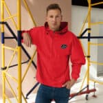 Bright red waterproof windbreaker jacket with Big Barber logo, ideal for casual and outdoor wear, showcased in a modern studio setting with yellow scaffolding background.