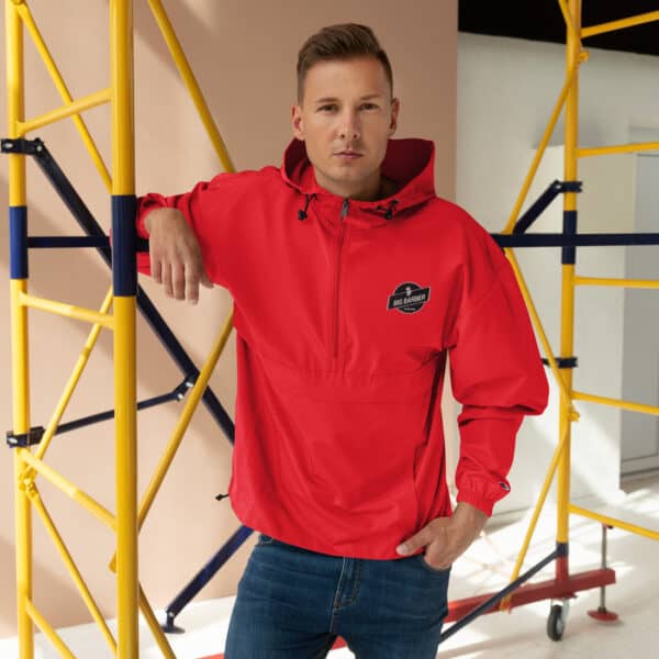 Bright red waterproof windbreaker jacket with Big Barber logo, ideal for casual and outdoor wear, showcased in a modern studio setting with yellow scaffolding background.